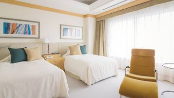 A hotel room with two beds, a chair, a nightstand, and a window with curtains.