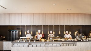 Un moderno montaje tipo buffet con cocineros preparando comida, una encimera de mármol y lámparas colgantes.
