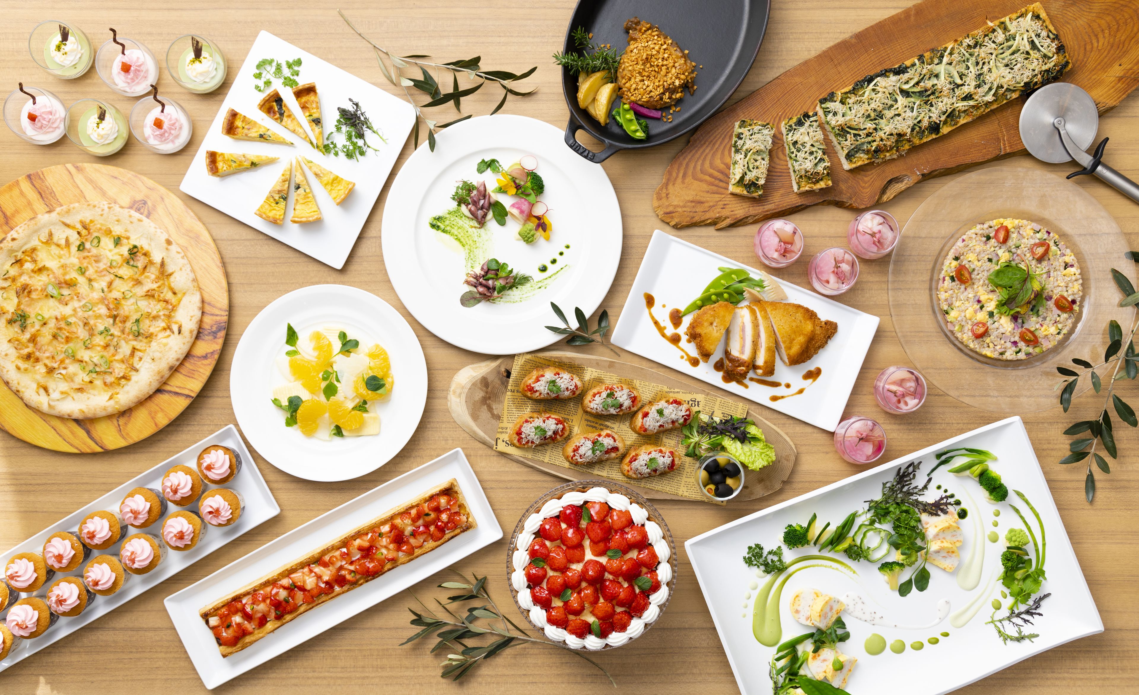 A variety of dishes on a wooden table, including pizza, a tart, and a salad.