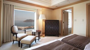 Habitación de hotel con dos camas, una silla, una mesita, una lámpara y vista al mar.