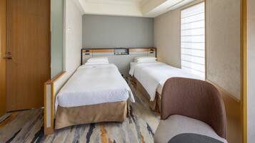 A hotel room with two beds, a wooden wardrobe, a carpeted floor, and a window with blinds.