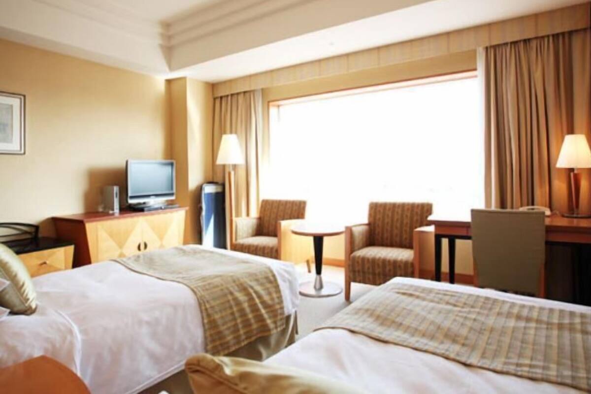 Una habitación de hotel con dos camas, televisión, escritorio y una silla.
