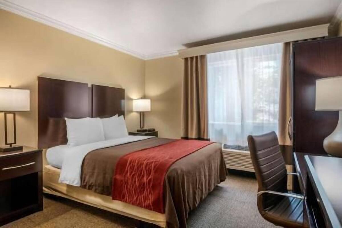 A hotel room with a bed, bedside lamps, a desk, and a chair.