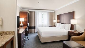 A hotel room with a bed, desk, chair, and a view of the outdoors.