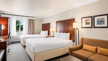 A hotel room with two beds, a desk, a chair, a sofa, and a lamp.