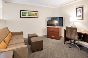 Habitación de hotel con sofá, escritorio, televisión y lámpara.