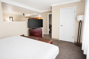Une chambre d’hôtel avec un grand lit, un téléviseur posé sur une commode en bois, une porte et un lampadaire.