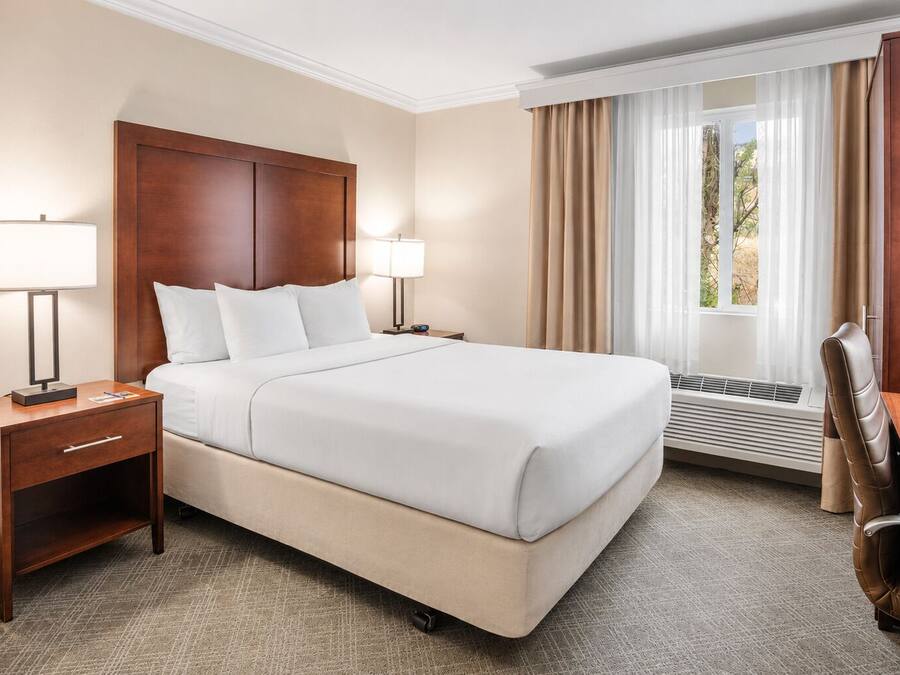 A hotel room with a large bed, bedside lamps, a desk, and a chair.