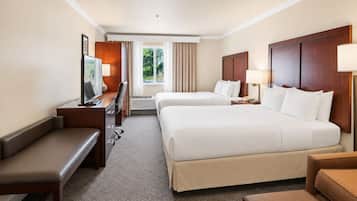 Une chambre d’hôtel avec deux lits, un bureau, une chaise, une télévision et une fenêtre avec des rideaux.