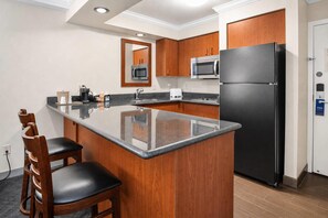 A compact kitchen with a central island, wooden cabinets, a black refrigerator, and a microwave. - Comfort Inn Columbia Gorge (The Dalles)