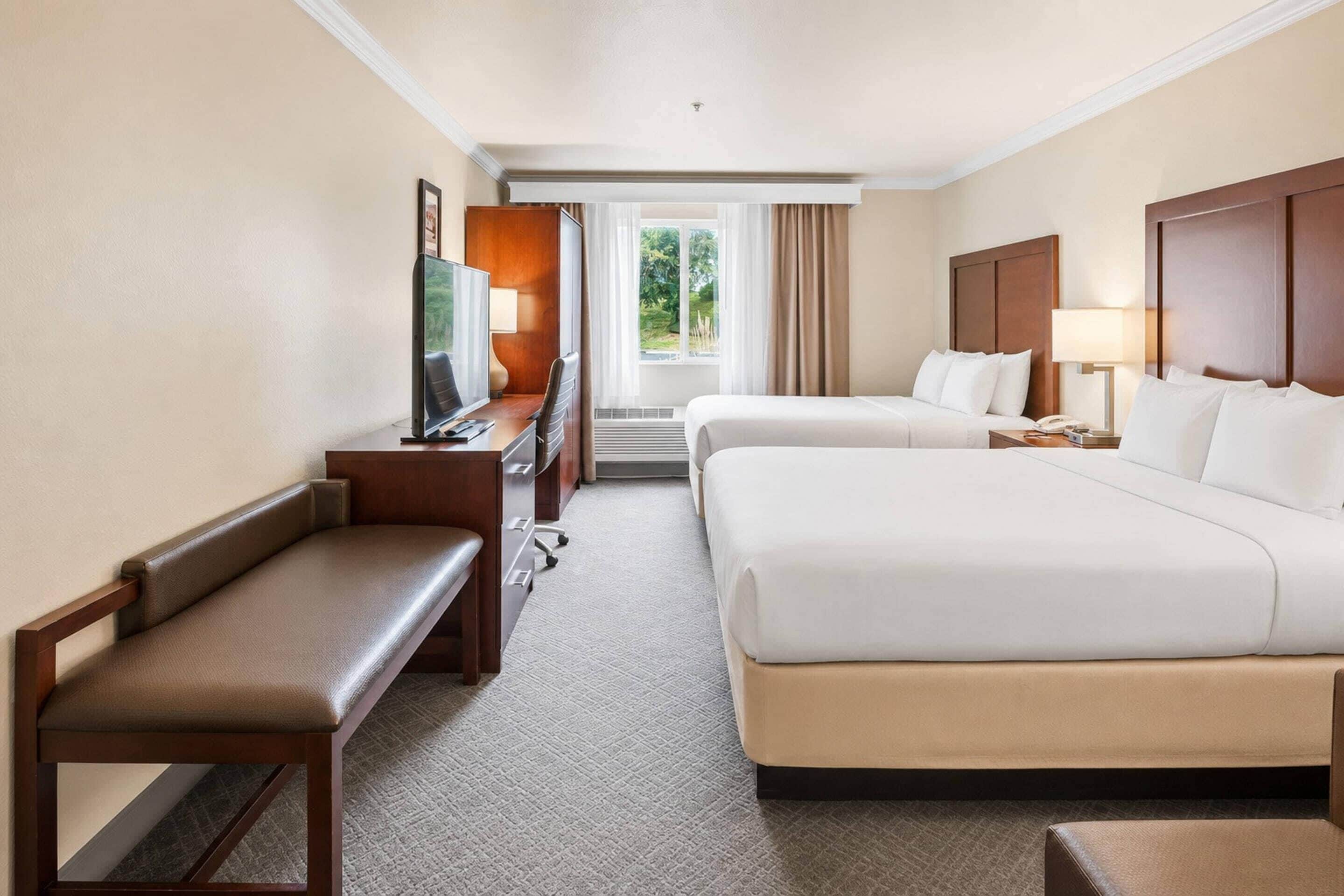 A hotel room with a bed, a desk with a TV, a chair, and a view of the outdoors.