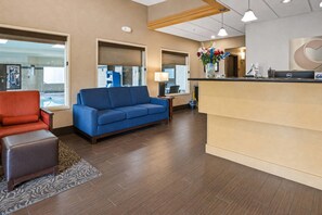 A hotel lobby with a reception desk, a blue sofa, a red armchair, and a patterned rug.
