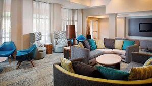 A modern living room with a sofa set, armchairs, a coffee table, and a flat-screen TV mounted on the wall. - Courtyard by Marriott West Palm Beach Airport (West Palm Beach)