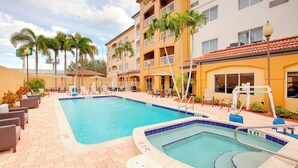 A hotel with a swimming pool, outdoor seating, and palm trees. - Courtyard by Marriott West Palm Beach Airport (West Palm Beach)