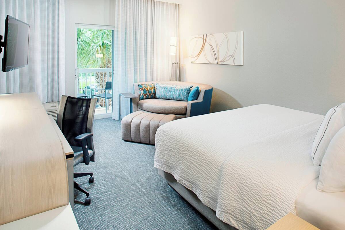 Ein Hotelzimmer mit Bett, Schreibtisch, Sessel, Sofa und Fernseher.