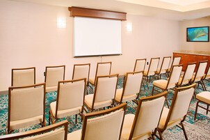 Un salón de conferencias con filas de sillas, una pantalla de proyección y un elemento decorativo en la pared.