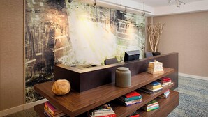A reception desk with a modern design, featuring a wooden finish and a built-in bookshelf filled with books. - Courtyard by Marriott West Palm Beach Airport (West Palm Beach)