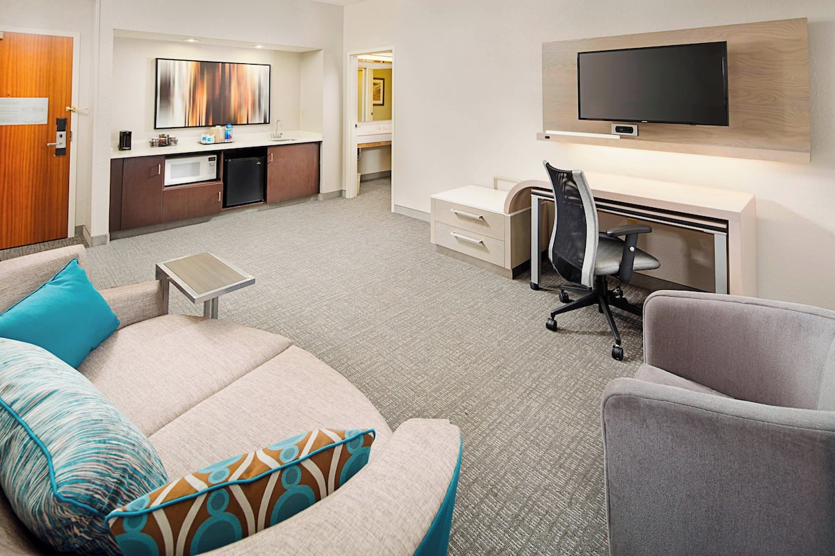 Ein Hotelzimmer mit einer Couch, einem Schreibtisch, einem Fernseher und einer Küchenzeile.