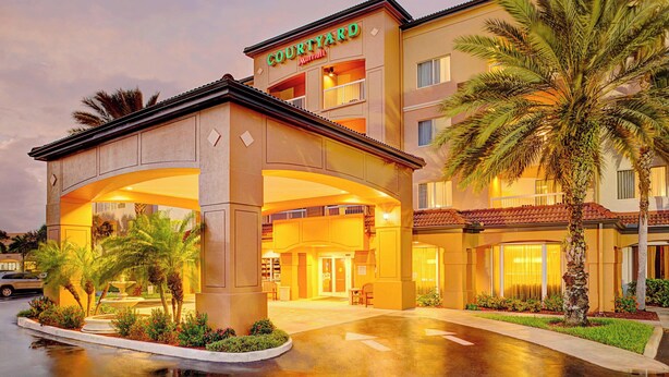 A Courtyard Marriott hotel entrance with a covered walkway, palm trees, and a well-lit facade. - Courtyard by Marriott West Palm Beach Airport (West Palm Beach)