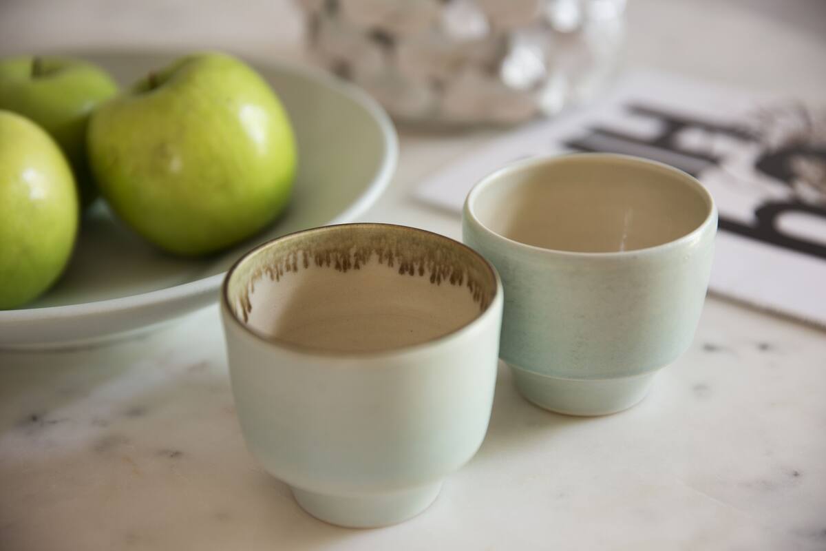 A plate with green apples and two ceramic cups on a marble surface.