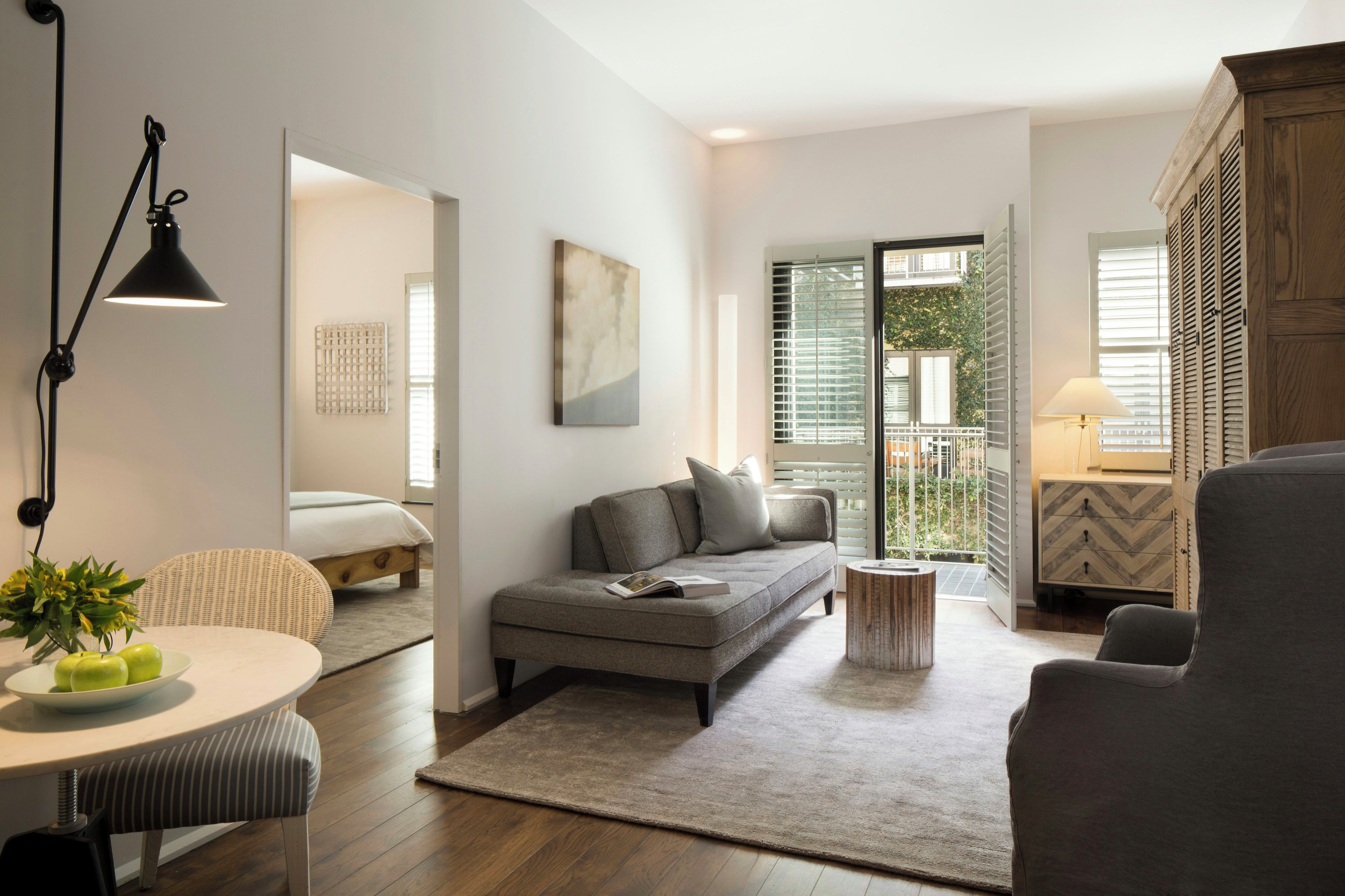 Una sala de estar moderna con un sofá, una mesa de comedor con manzanas, una lámpara y vistas al exterior a través de una ventana.