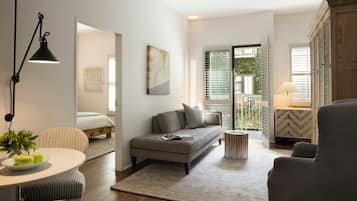 Una sala de estar moderna con un sofá, una mesa de comedor con manzanas, una lámpara y vistas al exterior a través de una ventana.