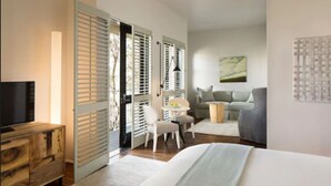 Habitación de hotel con cama, escritorio, silla, televisión y ventana con persianas.