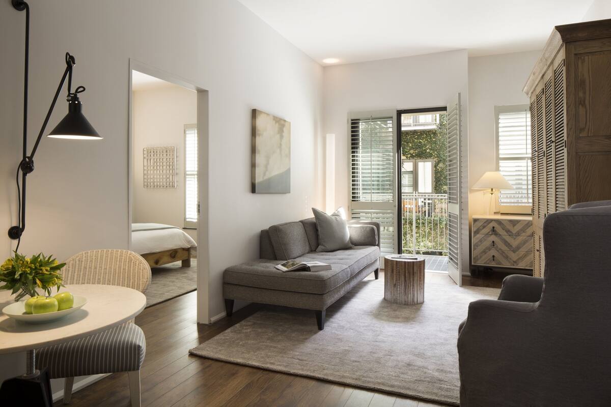A modern living room with a sofa, a dining table with apples, a lamp, and a view of the outdoors.