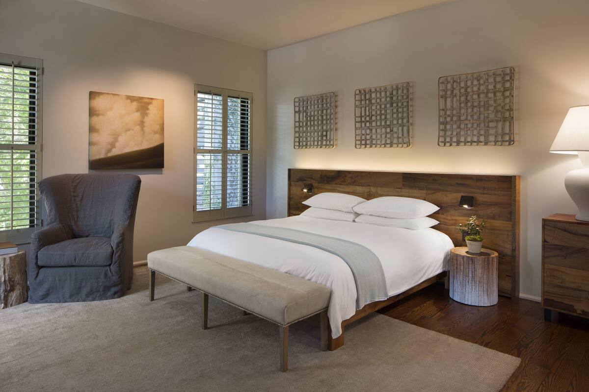 A bedroom with a large bed, a chair, a wooden headboard, and artwork on the walls.