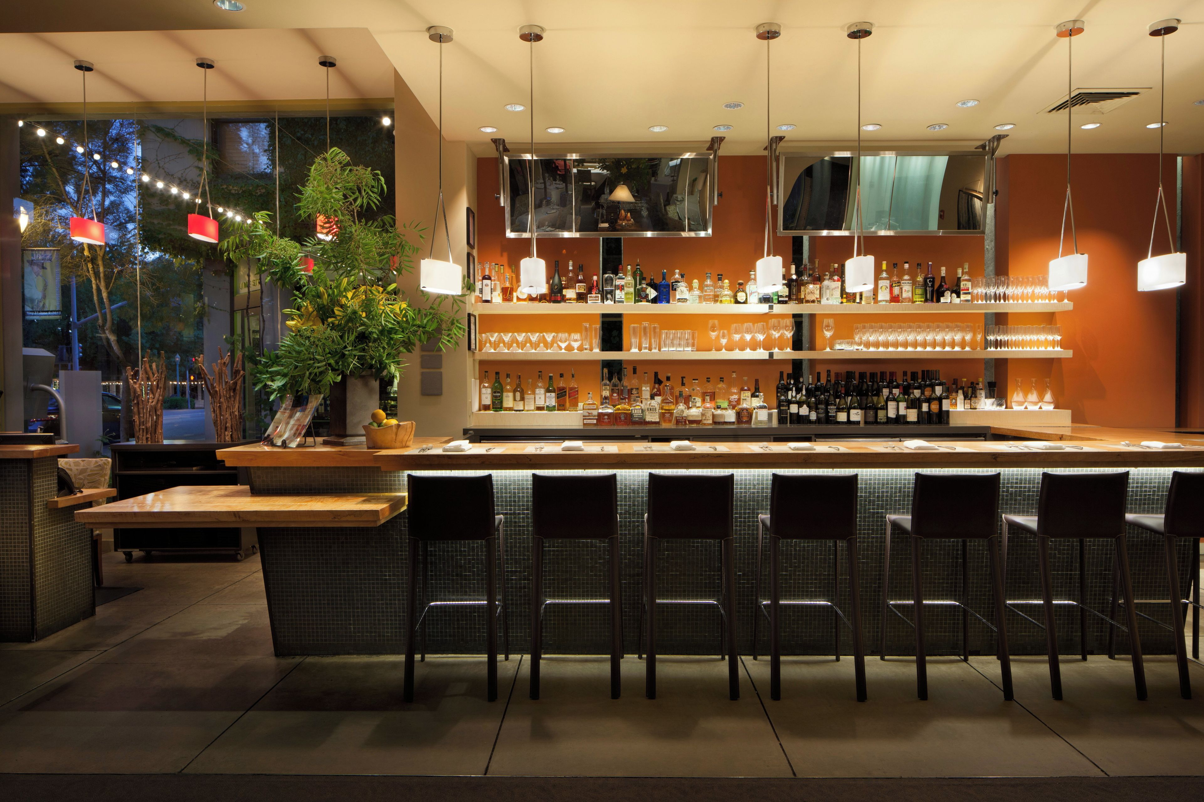 A bar area with a counter, multiple shelves of bottles, glasses, and a seating area with chairs.