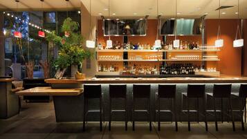 A bar area with a counter, multiple shelves of bottles, glasses, and a seating area with chairs.