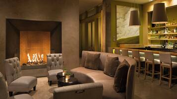 A modern lounge area with a fireplace, comfortable seating, and a bar with a variety of bottles.