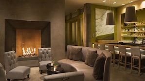 Un área de estar moderna con chimenea, asientos cómodos y un bar con estantes llenos de botellas.