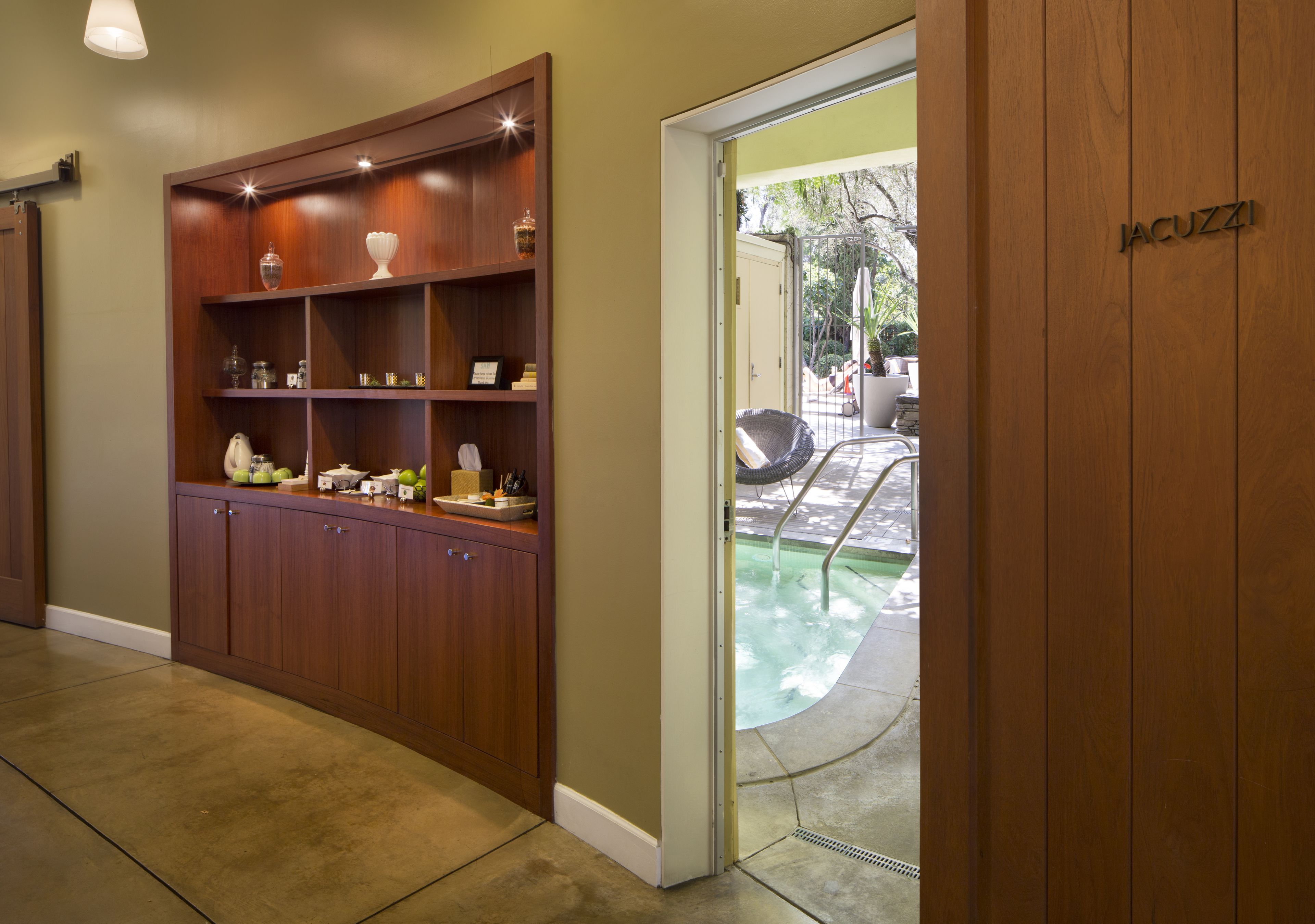 A wooden cabinet with shelves, a glass door leading to a pool area, and a sign reading "JACUZZI".