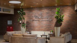 Vestíbulo de WestCord Aparthotel Boschrijck con sofás de cuero, pared de ladrillo y plantas en macetas.
