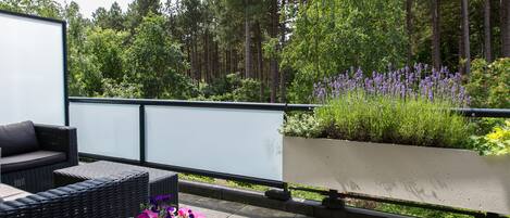 Ein Balkon mit Korbmöbeln, einem Blumenkasten und Blick auf einen Wald.