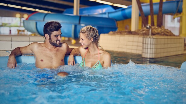 Una pareja en un jacuzzi con un tobogán de agua al fondo.