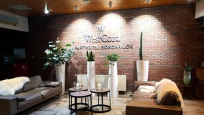 Un espacio lounge moderno con pared de ladrillo, dos sofás, mesas redondas y plantas en macetas.