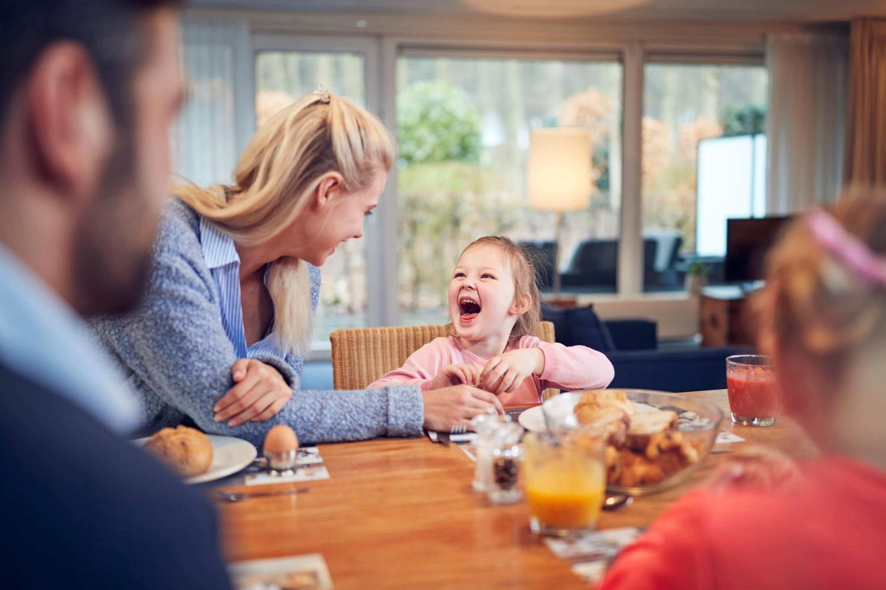 Una familia desayunando en una mesa con alimentos, un ordenador portátil y vistas al exterior.