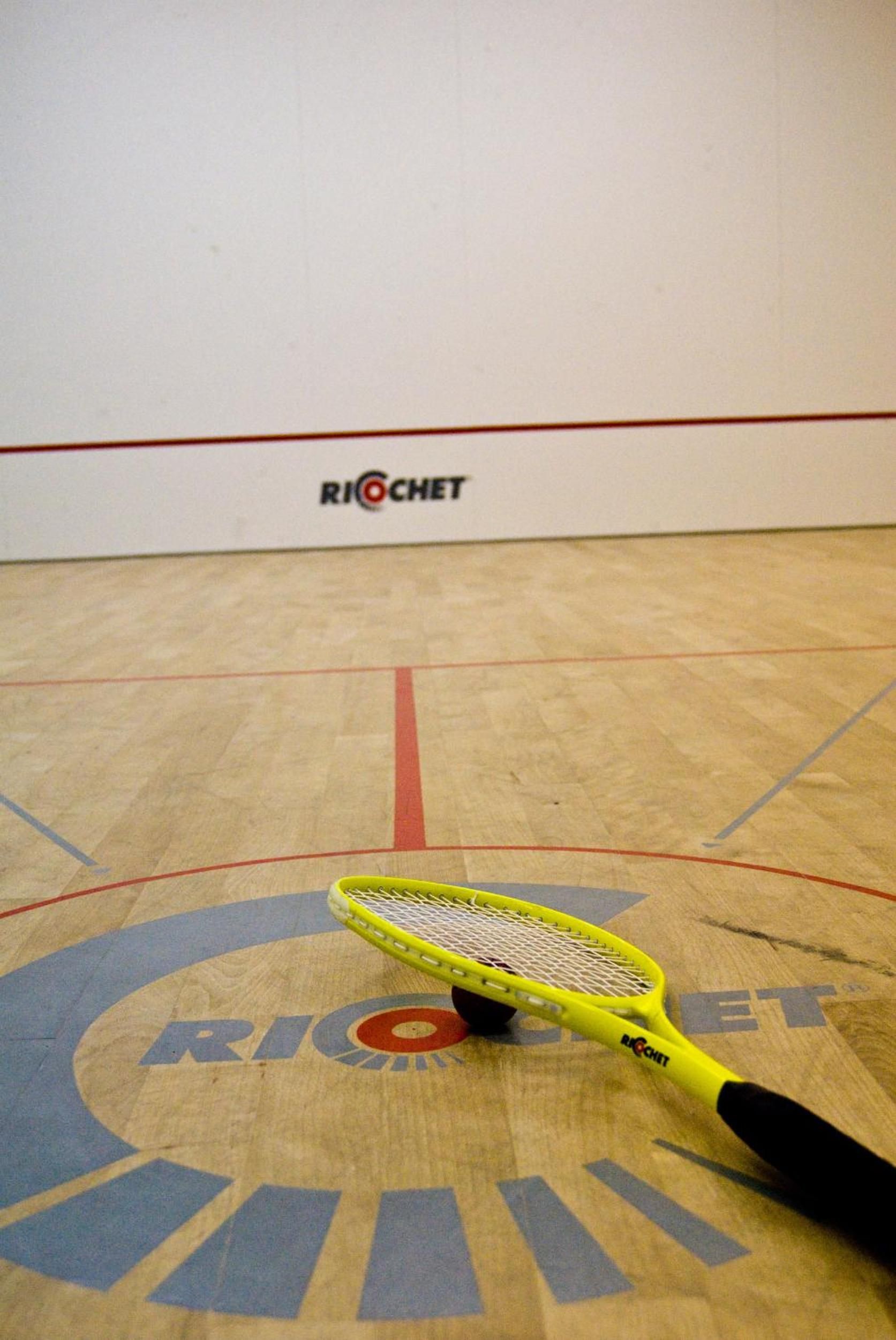 A squash court with a yellow racket on the floor.