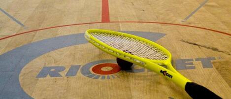 A squash court with a yellow racket on the floor.