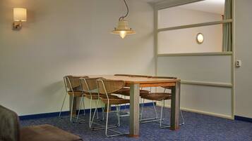 Une pièce comprenant une table à manger, quatre chaises en osier, un luminaire suspendu et une porte dotée d’un panneau en verre dépoli.