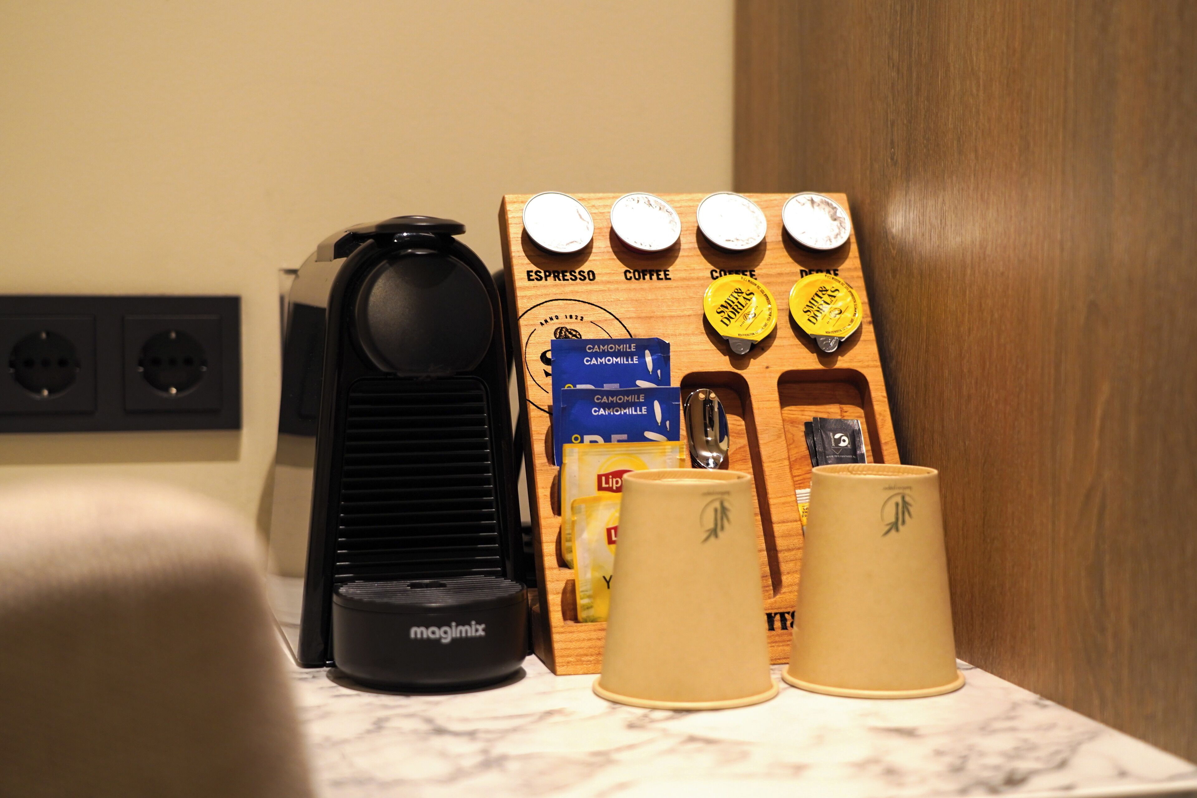 Una cafetera, un molinillo de café Magimix y un dispensador de cápsulas de café sobre una encimera de mármol.
