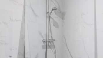 A glass-enclosed shower with a handheld showerhead and a wall-mounted faucet.