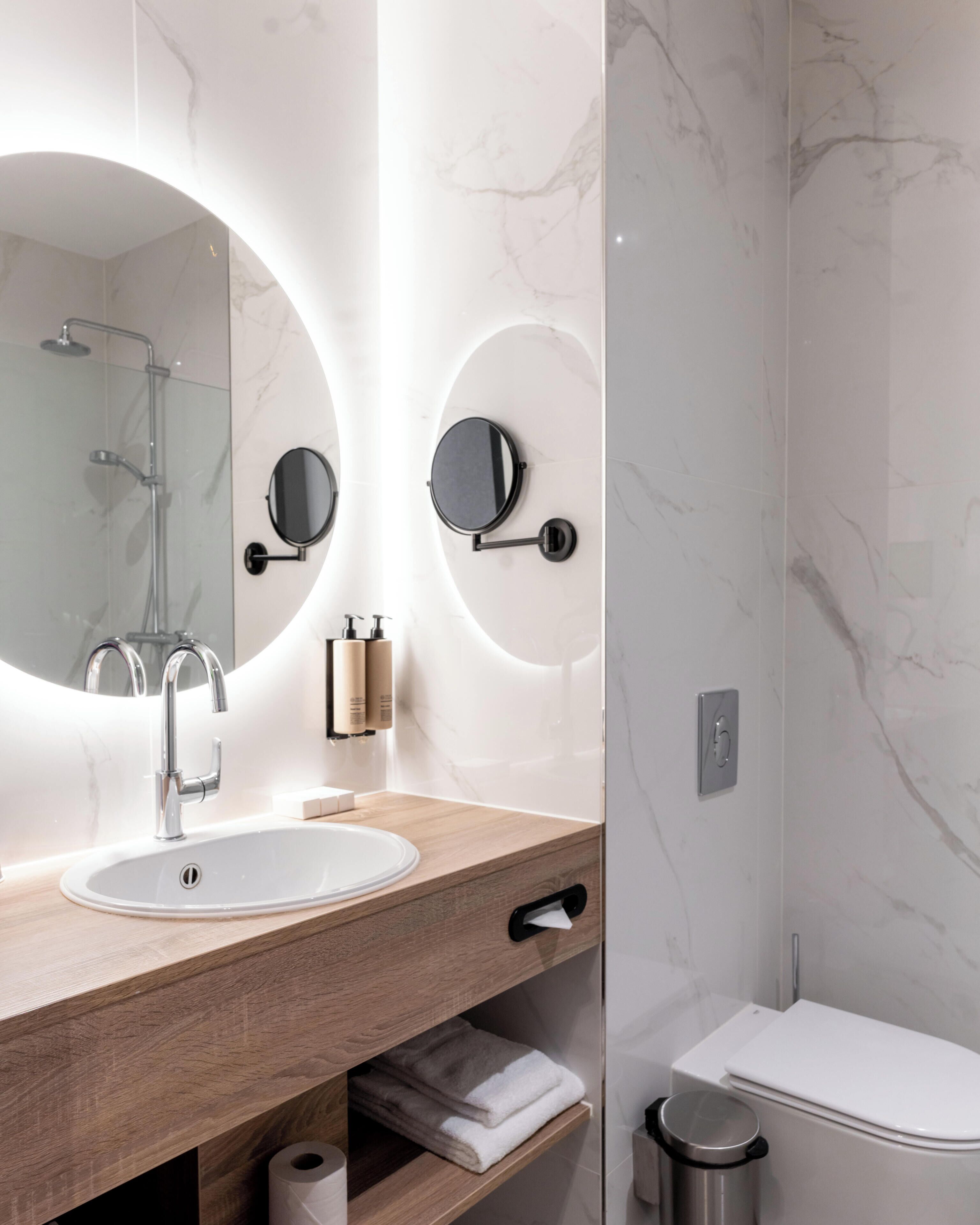 A modern bathroom with a marble vanity, a round mirror, a shower, and a toilet.