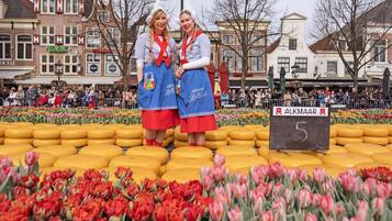 Dos personas frente a un expositor de queso amarillo y tulipanes rojos, con un letrero que dice "ALKMAAR 5".