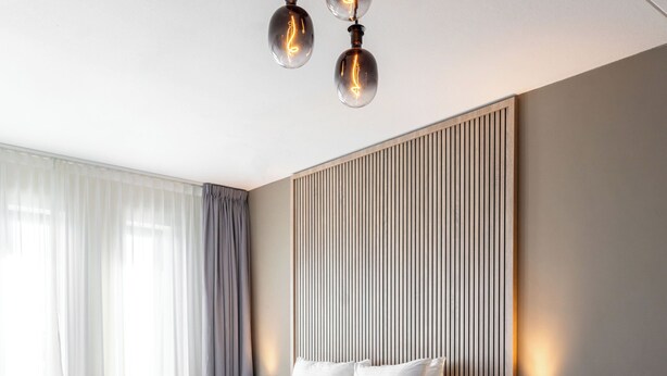 Quarto de hotel moderno com uma cama grande, mesas de cabeceira, uma escrivaninha e uma cadeira.