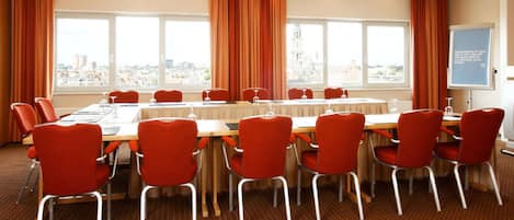 Ein Konferenzraum mit einem langen Tisch, roten Stühlen und großen Fenstern mit Vorhängen.