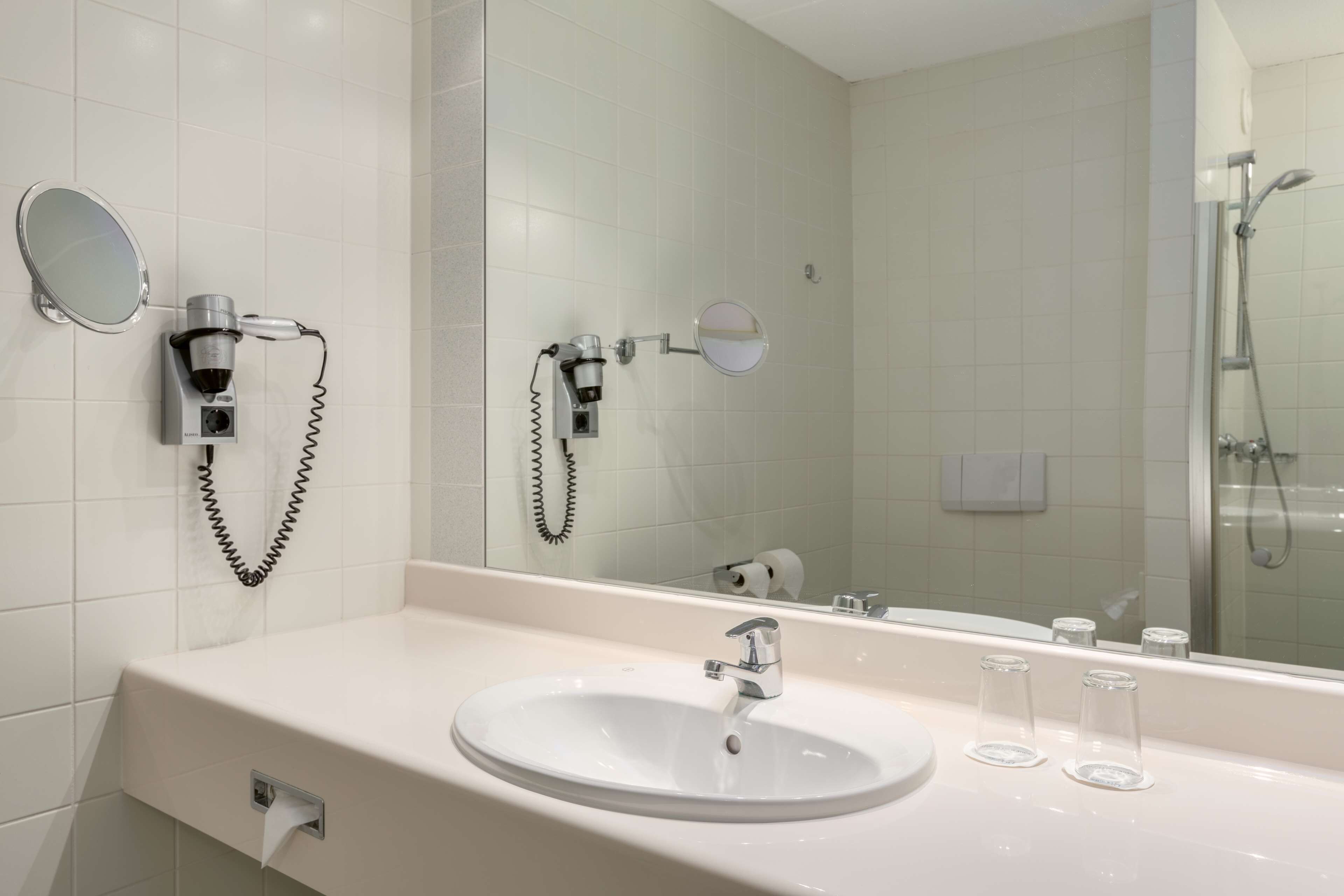 A bathroom with a white sink, a mirror, a hairdryer, and a shower.