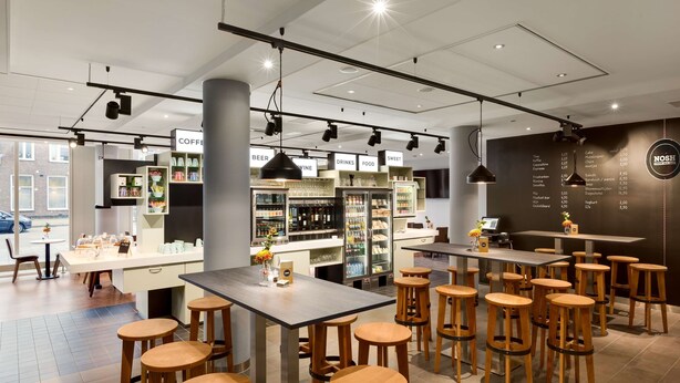 Un café moderno con taburetes de madera, una barra de café y una pizarra de menú.